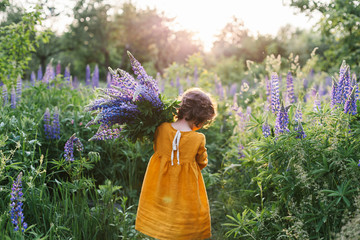 Adorable curly little girl wearing mustard linen dress with llupine flowers bouquet