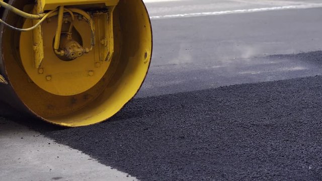 Close-up of an asphalt rink lays new asphalt on the road. Repair of roads. The repair work of industrial machines in the city. 4K.