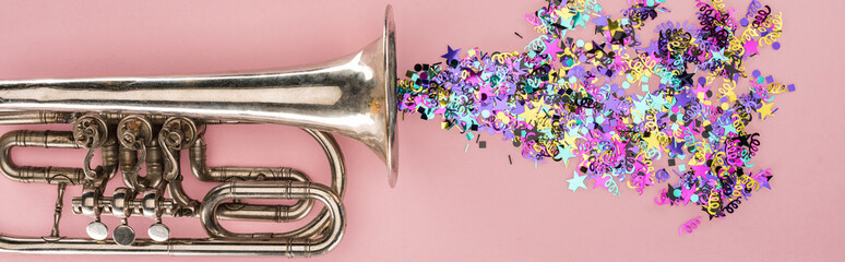 Panoramic shot of trumpet and colorful confetti on pink background