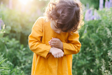 Adorable little girl wearing mustard linen dress with ladybug among lupine flowers