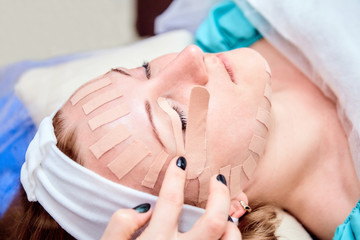 Face aesthetic taping. Facial skin care. Young woman lying with tape applications on face. Non-invasive anti-ageing lifting method for reduction of wrinkles on the forehead and the outer eye corners