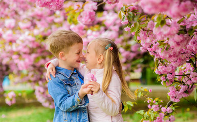 Romantic babies. Tender love feelings. Couple kids on flowers of sakura tree background. Little girl enjoy spring flowers. Giving all flowers to her. Surprising her. Kids enjoying pink cherry blossom