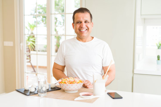Middle age man eating asian food with chopsticks at home with a happy and cool smile on face. Lucky person.
