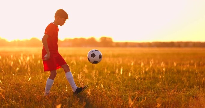 Boy football player at sunset juggling the ball in the field