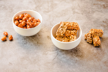 Gozinaki bars (Georgian Christmas confection) made of sunflower seeds and honey. Peanuts in sugar in white bowl and on gray background. Copy space for text