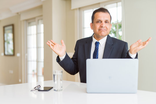 Middle age business man working with computer laptop clueless and confused expression with arms and hands raised. Doubt concept.