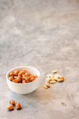 Peanuts in sugar in white bowl and on gray background. Selective focus. Copy space for text.