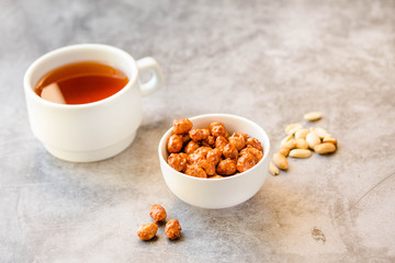 Peanuts in sugar in white bowl and on gray background. Horizontal. Copy space for text.