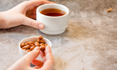 Dessert bars made of sunflower seeds  in a honey caramel. Gozinaki - traditional Georgian confection. Caramelized peanuts in white bowl and on gray background. In the hands of a young woman.