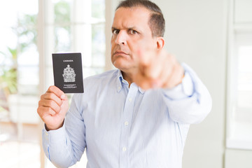 Middle age man holding holding Canadian passport pointing with finger to the camera and to you, hand sign, positive and confident gesture from the front