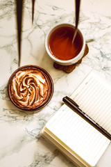 Opened notebook with blank area, pen and a cup of black tea on a white marble table in morning time.