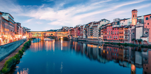Picturesque evening cityscape of Florence with Old Palace (Palazzo Vecchio or Palazzo della Signoria) on background and Ponte Vecchio bridge over Arno river. Colorful night panorama of Italy, Europe.