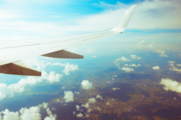 Fototapeta premium Right wing of flying passenger plane above clouds and green ground