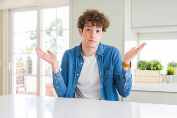 Young handsome man wearing casual denim jacket at home clueless and confused expression with arms and hands raised. Doubt concept.