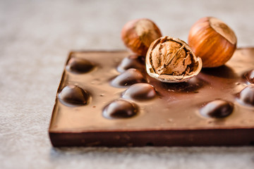 Dark chocolate bar with hazelnuts in the shell on gray background, closeup. Copy space for text.