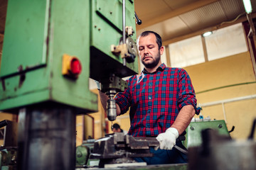 Worker using drill press in factory