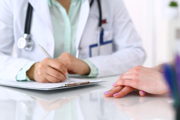 Doctor and patient talking while sitting at the desk in hospital office, close-up of human hands. Medicine and health care concept