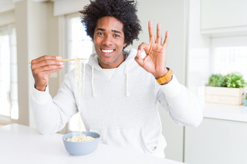 African American man eating asian noodles using chopsticks at home doing ok sign with fingers, excellent symbol