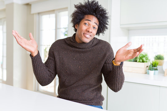 African American man wearing winter sweater clueless and confused expression with arms and hands raised. Doubt concept.