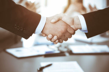 Business people shaking hands at meeting while theirs colleagues clapping and applauding. Group of unknown businessmen and women in modern white office. Success teamwork, partnership and handshake