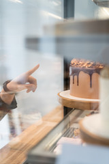 slice of chocolate dessert in the window of the pastry cafe. The girl shows the index finger on a piece of cake.