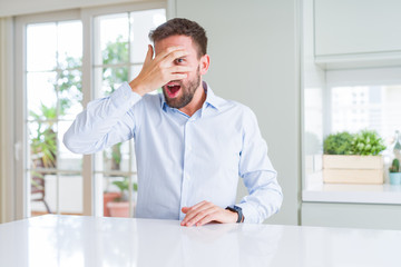 Handsome business man peeking in shock covering face and eyes with hand, looking through fingers with embarrassed expression.