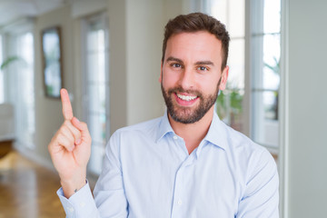Handsome business man with a big smile on face, pointing with hand and finger to the side looking at the camera.