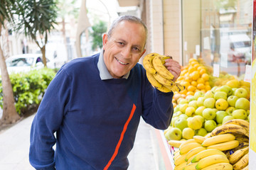 Handsome senior man at fruit store stand smiling buying fresh organic groceries