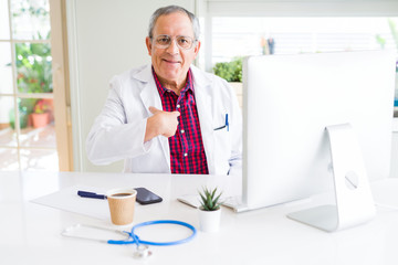 Handsome senior doctor man doing research using laptop looking for a cure at the clinic with surprise face pointing finger to himself