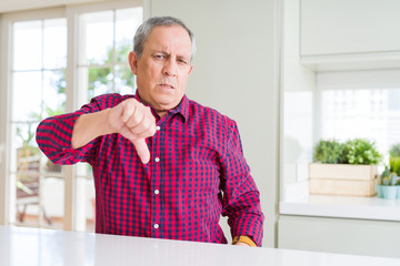 Handsome senior man at home looking unhappy and angry showing rejection and negative with thumbs down gesture. Bad expression.