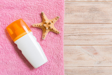 Top view of summer beach staff with copy space. Seashells or seastar, a bottle of suncream and pink towel on wooden background. Summer vacation concept
