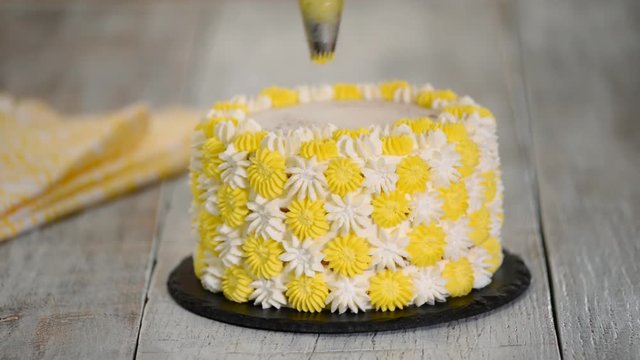 Female chef with pastry bag squeezing cream on cake at kitchen. Woman preparing a cake at home.