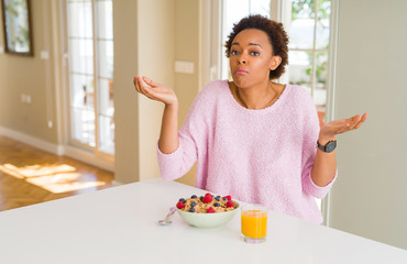 Young african american woman having healthy breakfast in the morning at home clueless and confused...