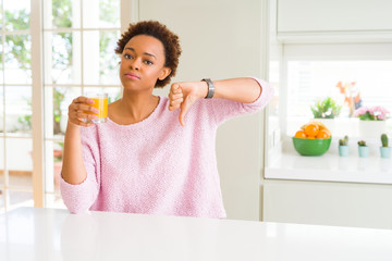 Young african american woman driking orange juice at home with angry face, negative sign showing...