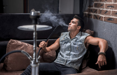 Sexy guy relaxes in a hookah in the shisha bar.