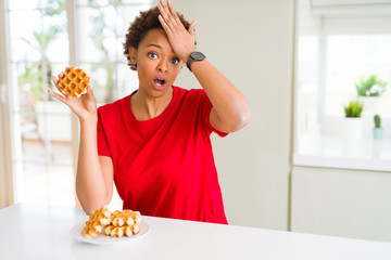 Young african american woman eating sweet waffle stressed with hand on head, shocked with shame and surprise face, angry and frustrated. Fear and upset for mistake.