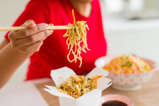 Close up of young woman eating noodles from delivery box using choopsticks