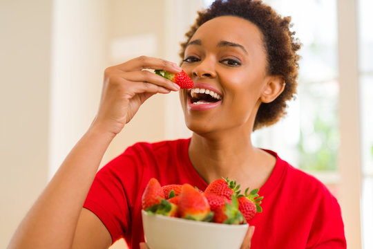 Beautiful young african woman with afro hair eating fresh strawberries
