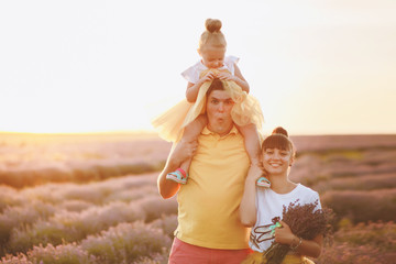 Young family in yellow clothes walk on purple lavender flower meadow field background, have fun, play with little cute child baby girl. Mother father, small kid daughter. Outdoors summer day concept.