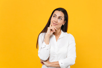 Portrait of pensive pretty young woman in white shirt put hand prop up on chin, looking aside isolated on bright yellow orange wall background in studio. People lifestyle concept. Mock up copy space.