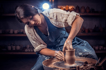 Charming female master molding a vase of clay on a potter's wheel. Handicraft production.