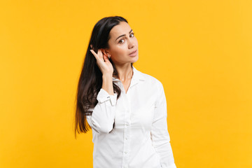Portrait of attractive young woman in white casual shirt looking camera try to hear you with hand...