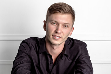 Fototapeta premium Pensive young handsome man in black shirt sitting on the chair and looking at camera