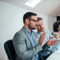 Two handsome businessmen clapping hands and talking on a meeting.