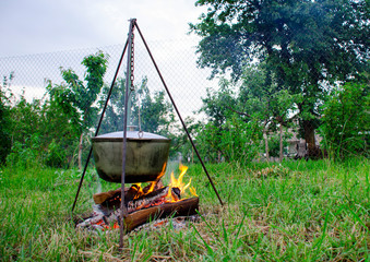 A man's hand kindles a fire under a pan, which stands on a fire.