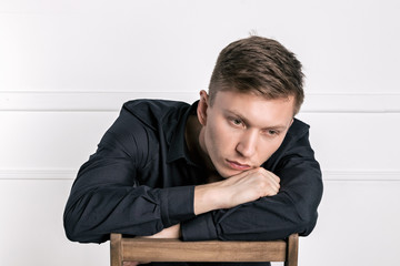 Pensive young handsome man in black shirt sitting on the chair and looking at camera