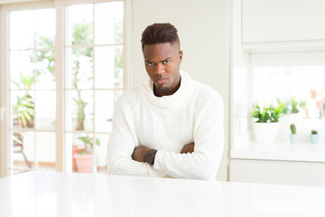 Handsome african american man on white table skeptic and nervous, disapproving expression on face with crossed arms. Negative person.