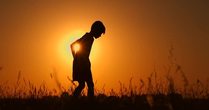 Silhouette of a boy playing football at sunset. A boy juggles a ball in the field at sunset