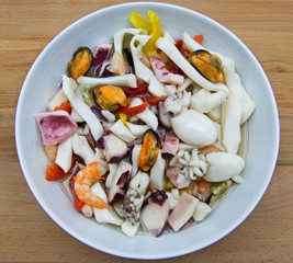 White dish of mixed mediterranean seafood salad on wooden table