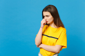 Portrait of displeased pensive young woman in vivid casual clothes looking aside keeping hand near face isolated on bright blue wall background in studio. People lifestyle concept. Mock up copy space.